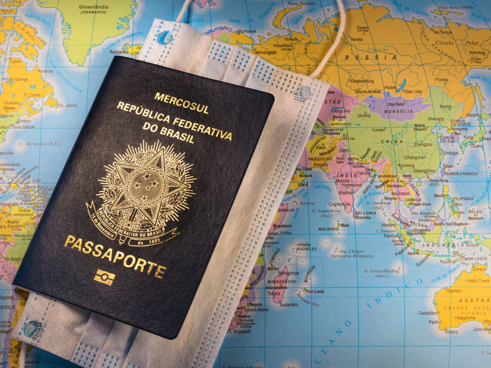 A top view shot of Brazilian passport with a vaccine syringe and facemask on a world map as background